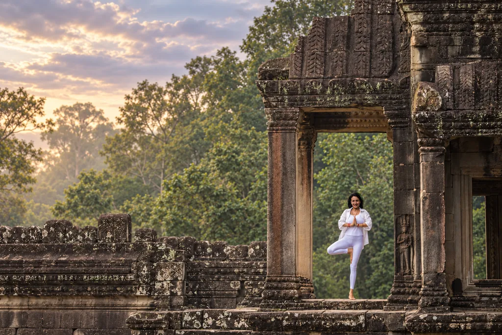 Marielisa Padilla in tree pose in a sandstone temple doorway at Angkor, early morning light through the trees